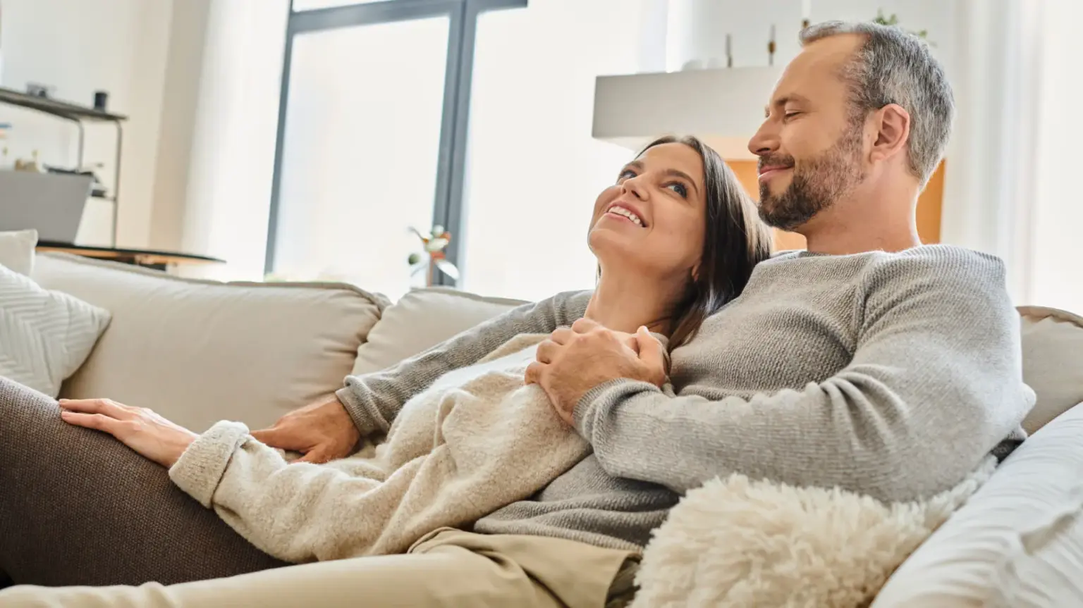 A husband and wife laying back on the couch happy in their clean home,