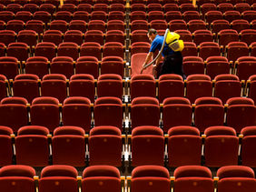 A cleaner vacuuming between rows of seats in a theatre.